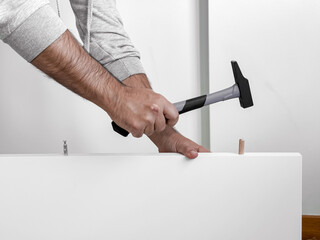 Male adult Caucasian assembling furniture with hammer and wooden pegs