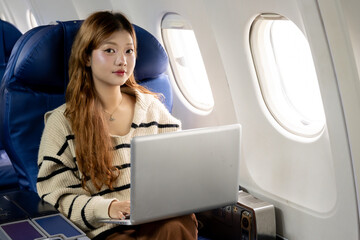 Asian woman sitting watching a movie on her laptop on an airplane while traveling somewhere during her vacation.