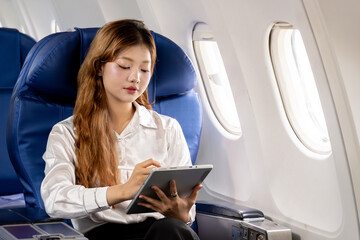 Asian businesswoman using her tablet while on a business trip on an airplane.