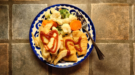 plate consisting of breaded codfish, mixed veggies and thick cut steak fries with ketchup 