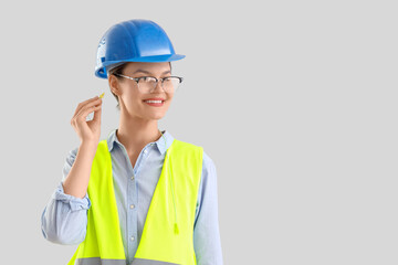 Female builder inserting earplugs on light background
