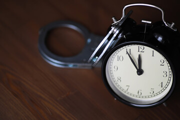 Time and Consequence: Black Clock Handcuffed on Wooden Surface Reflecting Urgency and Punishment