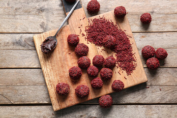 Board with delicious chocolate truffles, sprinkles and spoon of chocolate paste on wooden background