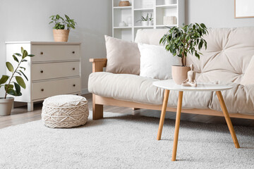 Interior of light living room with beige sofa, table and drawers