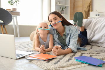 Nanny and funny little girl with pens lying on floor while studying in bedroom