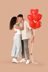 Loving young couple with heart-shaped balloons hugging on beige background. Valentine's Day celebration