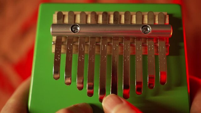 Close-up of a musician playing a green kalimba with metal tines, illuminated by a red light, creating a vibrant and captivating visual contrast