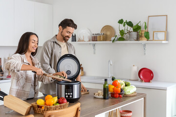 Young couple with multi cooker preparing food in kitchen