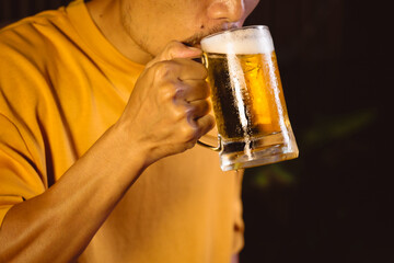 A man's hand lifts a beer glass in the quiet aftermath of a night party, capturing a solitary moment of reflection under dim lights and the lingering echo of celebration.