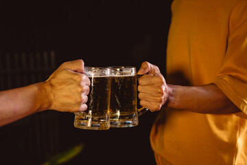 A man's and woman's hands raise beer glasses group in a lively night party, surrounded by family and friends. The evening is filled with warmth, laughter, and joyful celebration.
