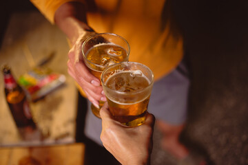 A man's and woman's hands raise beer glasses group in a lively night party, surrounded by family and friends. The evening is filled with warmth, laughter, and joyful celebration.