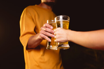 A man's and woman's hands raise beer glasses group in a lively night party, surrounded by family and friends. The evening is filled with warmth, laughter, and joyful celebration.
