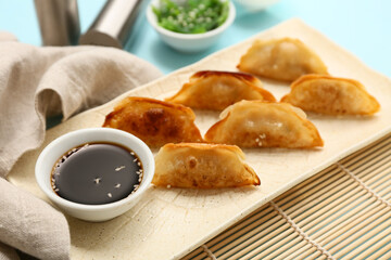 Plate with fried Japanese gyoza and bowl of soy sauce on blue background, closeup