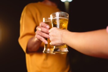 A man's and woman's hands raise beer glasses group in a lively night party, surrounded by family and friends. The evening is filled with warmth, laughter, and joyful celebration.