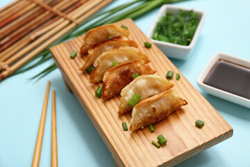 Wooden stand with fried Japanese gyoza, green onion and bowl of soy sauce on blue background