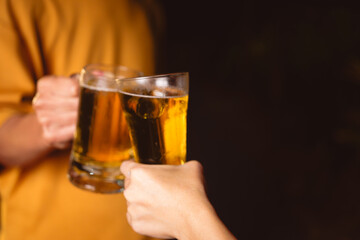 A man's and woman's hands raise beer glasses group in a lively night party, surrounded by family and friends. The evening is filled with warmth, laughter, and joyful celebration.