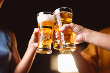 A man's and woman's hands raise beer glasses group in a lively night party, surrounded by family and friends. The evening is filled with warmth, laughter, and joyful celebration.