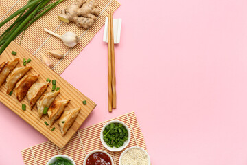 Wooden stand with fried Japanese gyoza, green onion and bowl of sauce on pink background