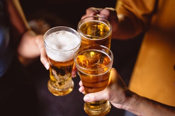 A man's and woman's hands raise beer glasses group in a lively night party, surrounded by family and friends. The evening is filled with warmth, laughter, and joyful celebration.