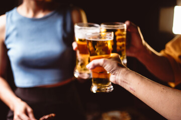 A man's and woman's hands raise beer glasses group in a lively night party, surrounded by family and friends. The evening is filled with warmth, laughter, and joyful celebration.
