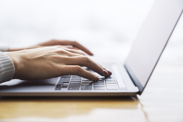 Female hands typing on a trendy laptop keyboard, with a blurry office scene in the background