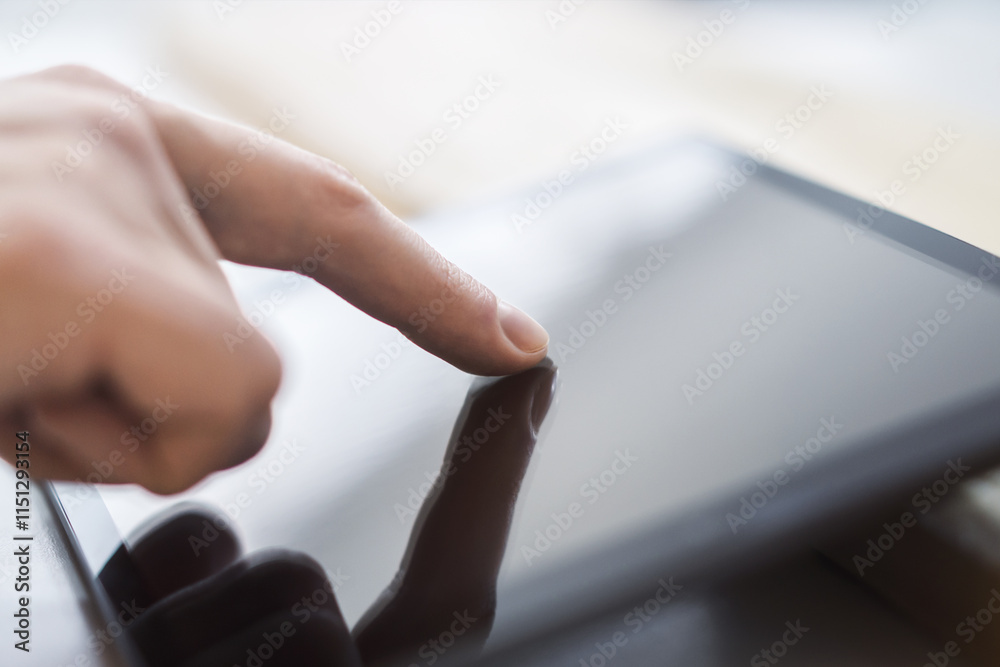 Poster man's finger operating a modern tablet device placed on a desk, within the blurry contours of a well