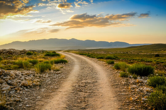 Rocky path through vast open landscape at sunset with distant mountains