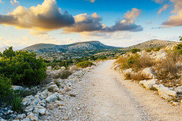 Scenic rocky pathway through rolling hills under vibrant cloudy sky