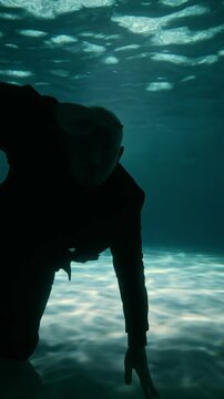 a bald man in a black suit swims underwater to the camera and peers into the darkness. Swims away from the camera underwater. The concept, the underwater search, the start of the competition. 4K