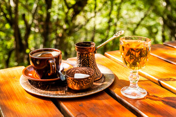 
Black coffee in a cup, vintage copper coffee pot and a glass of domestic brandy on a rustic wooden table