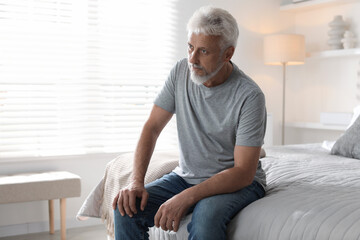 Lonely senior man sitting on bed at home