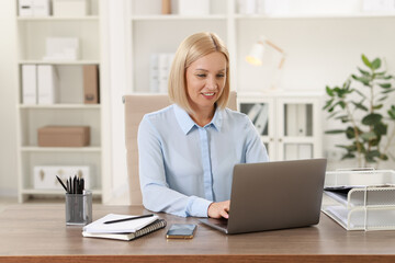 Smiling middle aged woman working with laptop at table in office