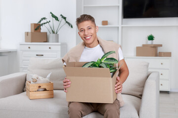 Happy man holding moving box with houseplant in new apartment. Housewarming party