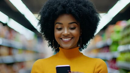 Happy woman using a smartphone while browsing for groceries in a lively supermarket, embracing the ease of modern technology