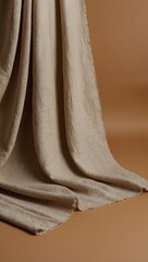 Soft beige linen fabric draping elegantly against warm brown background, creating a serene and minimalist aesthetic ideal for textile or interior design projects.