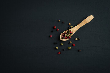 colorful peppercorns lie on a wooden spoon on a black background