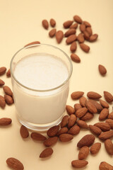 Fresh almond milk in glass and almonds on beige background. Healthy vegan plant based alternative milk replacer. Vertical photo