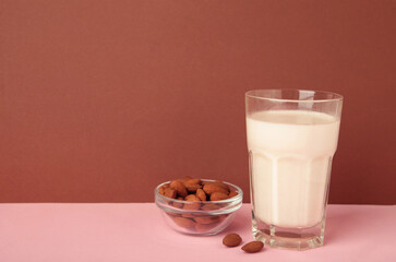 Fresh almond milk in glass and almonds on brown background. Healthy vegan plant based alternative milk replacer. Space for text
