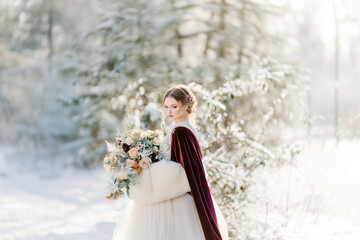 Elegant Bride in Vintage-Inspired Wedding Dress and Velvet Cape Posing Gracefully in Snowy, Romantic Setting