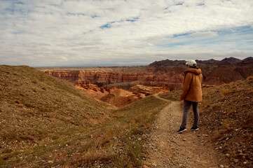 Fototapeta premium female tourist on the trail looking at the beautiful orange canyon mountains and cloudy sky