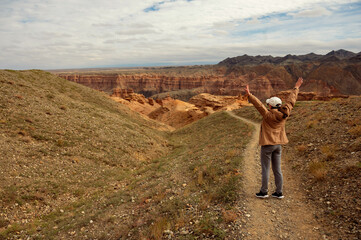 female tourist on the trail looking at the beautiful orange canyon mountains and cloudy sky