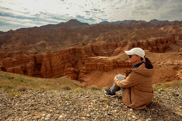 female tourist sits on a hill and looks at the beautiful orange canyon mountains and cloudy sky
