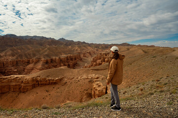 Naklejka premium female tourist on the trail looking at the beautiful orange canyon mountains and cloudy sky