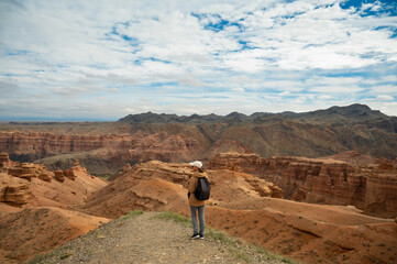 female tourist with backpack on hill looking at beautiful orange canyon mountains, rear view