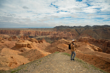 female tourist with backpack on hill looking at beautiful orange canyon mountains, rear view