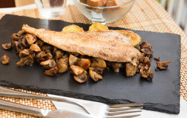 Fried trout fillet on pillow of fried champignon mushrooms on dark warm stone plate