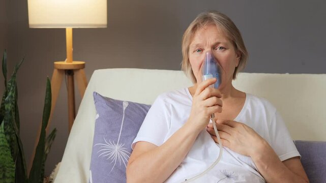 A woman sits comfortably in her living room, using a nebulizer to assist with her breathing