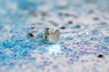 Elegant silver heart shape stud earring placed on a sparkling blue glitter background surface.