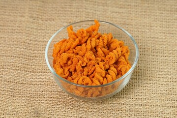 Spicy fried small macaroni crackers, on a brown cloth background, flat lay or top view, with studio lighting