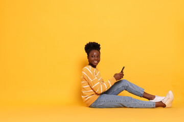 Happy woman with smartphone on yellow background. Space for text